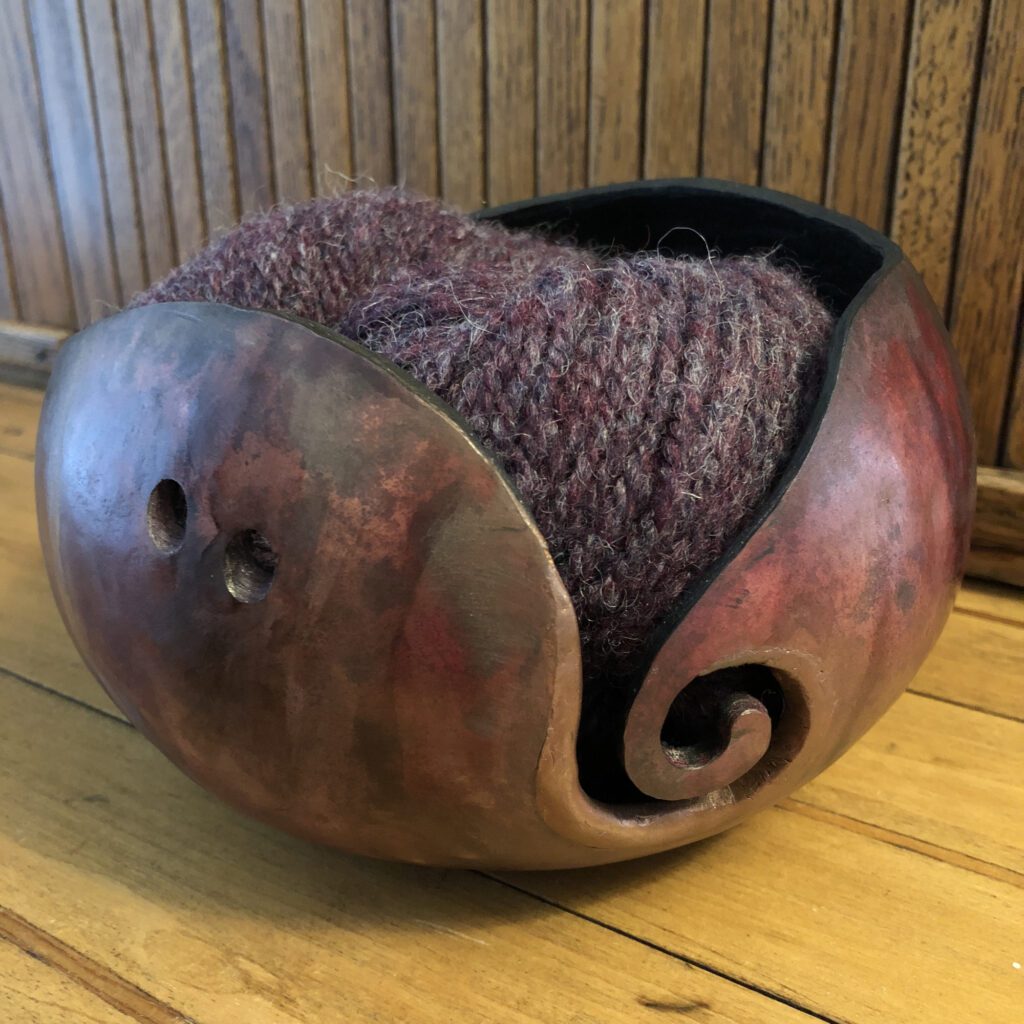 A bowl with yarn inside of it on the floor.