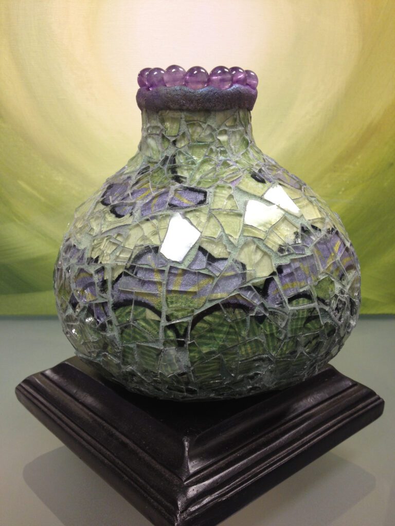 A vase with purple and green glass on top of a wooden stand.